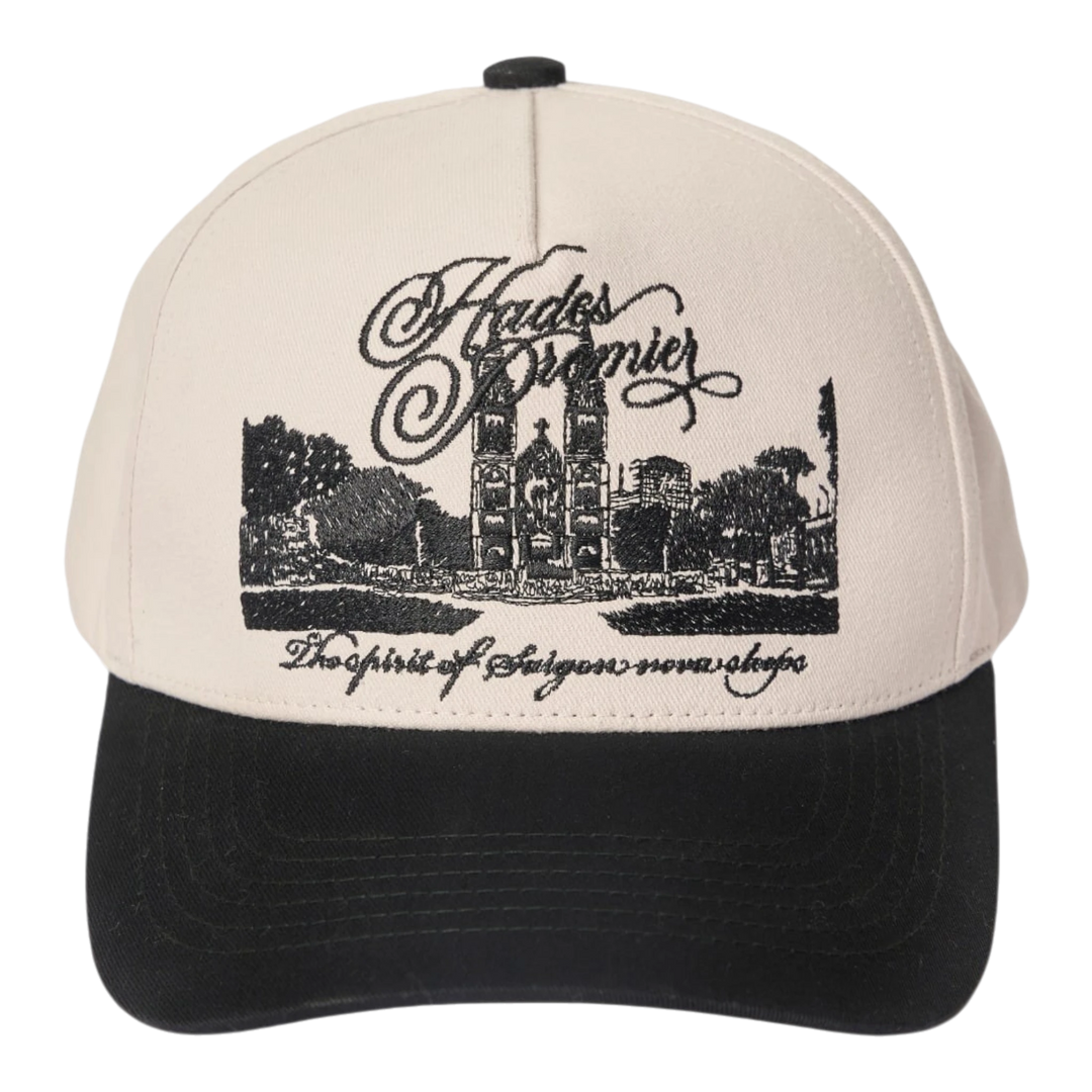 HADES Studio District 1 Cap: cream cotton cap with black brim, featuring embroidered Notre-Dame Cathedral Saigon and text.