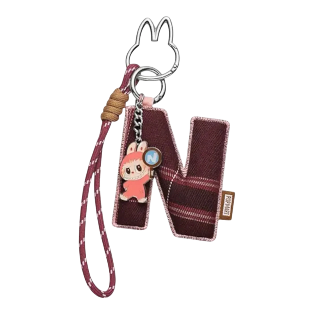HypeSelection Pop Mart Labubu 'N' letter pendant with plaid fabric and a small character charm. Features a keyring and strap.