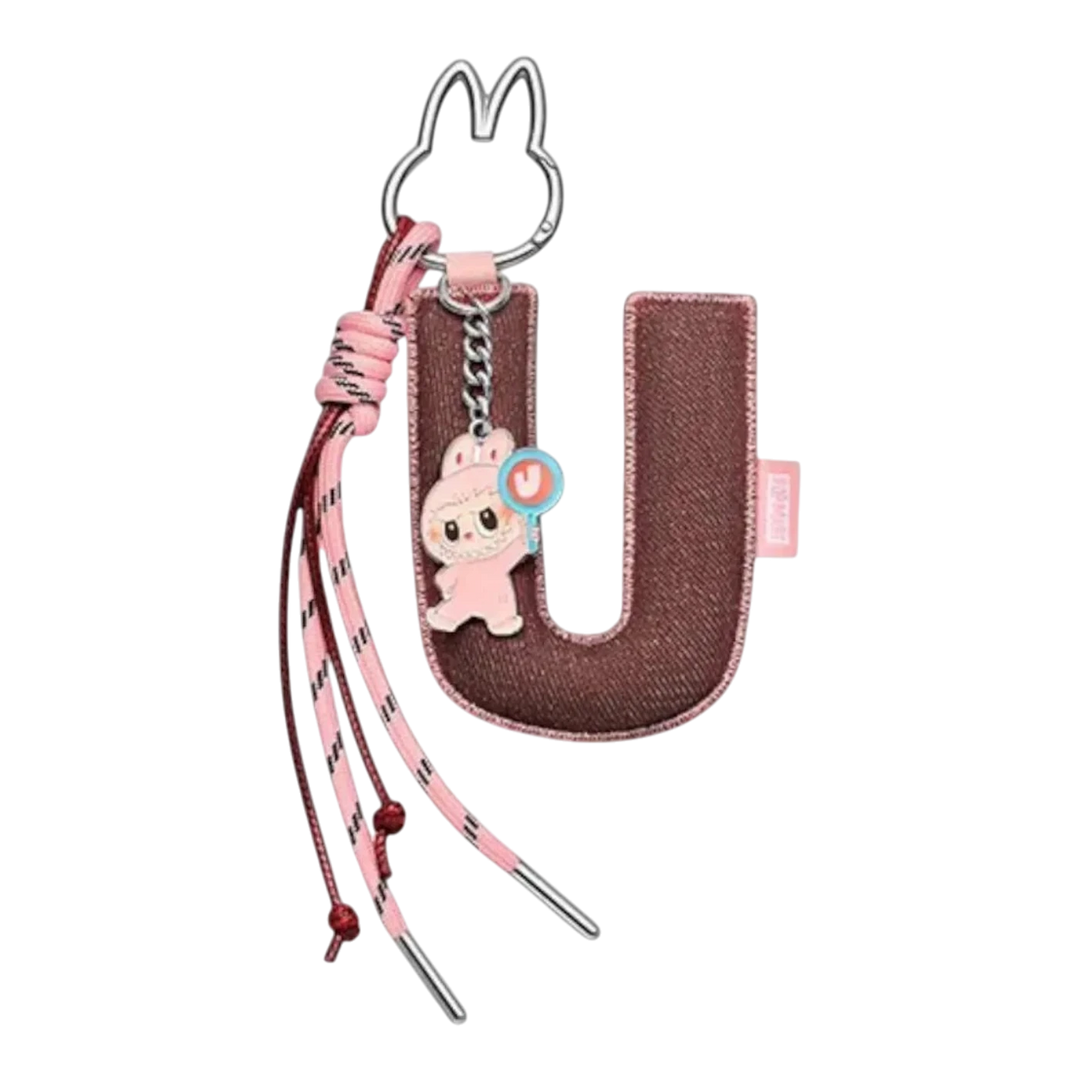 HypeSelection Pop Mart Labubu "U" letter pendant with pink plush toy and keychain. Brown fabric.
