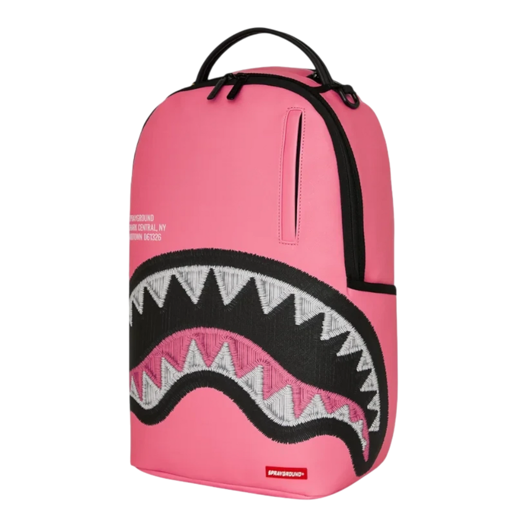 HypeSelection Sprayground pink backpack featuring a large embroidered shark mouth design and black zipper details.