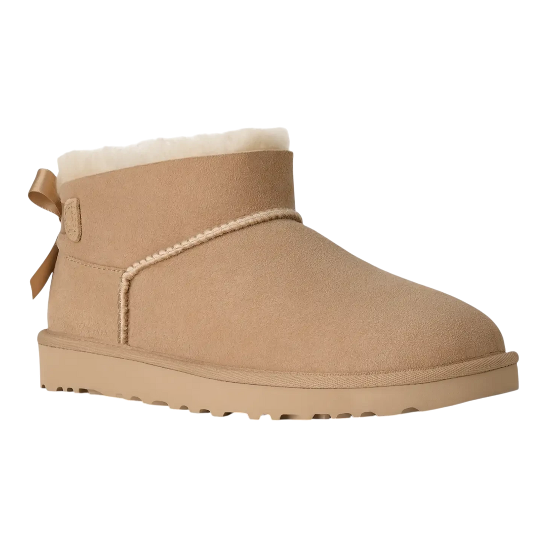HypeSelection UGG Ultra Mini Bailey Bow boot in sand suede with a plush wool lining and back satin bow detail.