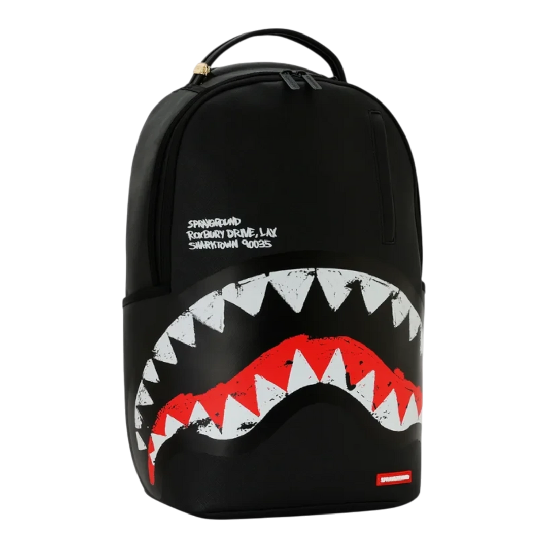 HypeSelection Sprayground black backpack featuring a bold white and red shark mouth graphic and embroidered text.