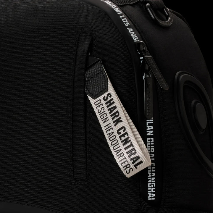 HypeSelection Sprayground Shark Central backpack featuring a black fabric exterior with branded zipper pull detail.